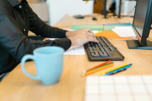 A person working at a desk with a keyboard, colored pencils, and a coffee mug.
